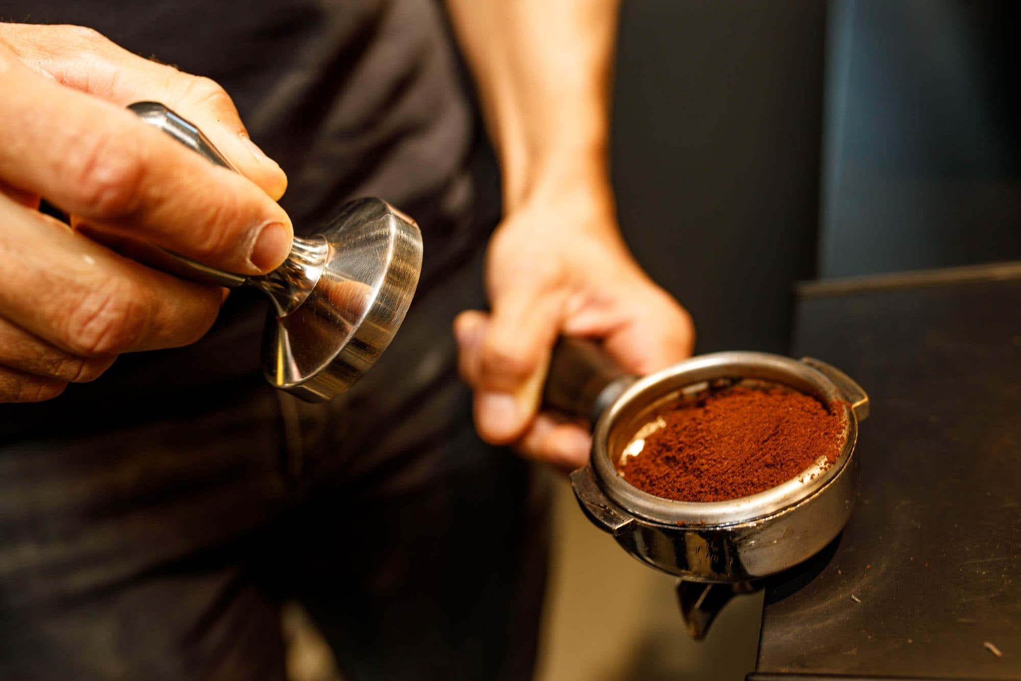 A barista tamps freshly ground coffee
